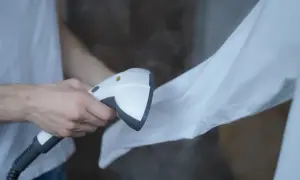 Para jak prasować koszulę: para z ręcznego parowca usuwa zagniecenia z białej tkaniny.