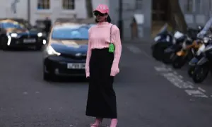 Różowy sweter do czarnej spódnicy, uzupełnione jaskrawą torebką i butami. Kobieta w czapce z daszkiem na ulicy.