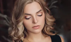 Delikatny, świąteczny makijaż podkreśla urodę blondynki. Jasne cienie na powiekach i subtelna szminka tworzą idealny look na zimowe przyjęcia.