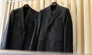 Dwa eleganckie garnitury wiszą na wieszakach. Jeden w prążki, drugi z subtelnym wzorem. Prasowanie garnituru to klucz do nienagannego wyglądu.