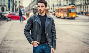 Młody mężczyzna w skórzanej kurtce i jeansach, stylizacja nawiązująca do moda męska lata 90. na tle miejskiej ulicy.