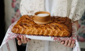 Tradycyjne powitanie chlebem i solą. Złocisty bochenek z ozdobnym wzorem, na nim drewniana solniczka.
