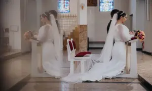 Panna młoda w białej sukni i welonie klęczy przy ołtarzu, trzymając bukiet. To symboliczny moment przenoszenia przez próg nowego życia.