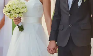 Para weselna trzymająca się za ręce. Panna młoda w białej sukni z bukietem róż. Zastanawiasz się, ile dać na wesele od 4 osobowej rodziny?