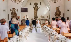Przebieg mszy ślubnej: para młoda stoi przed ołtarzem w kościele, otoczona gośćmi i kwiatowymi dekoracjami.