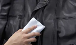 Dłoń z białym materiałem delikatnie naciera czarną skórzaną kurtkę, pokazując domowe sposoby, czym natłuścić kurtkę skórzaną.