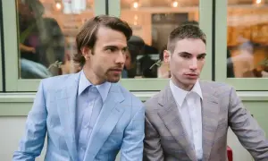 Dwóch mężczyzn w eleganckich garniturach w kratę. Wyłogi marynarki jednego są błękitne, drugiego beżowe.