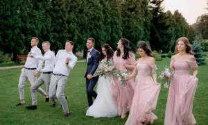 Para młoda i drużyna weselna w eleganckim ubiorze na ślub, idący przez trawnik.