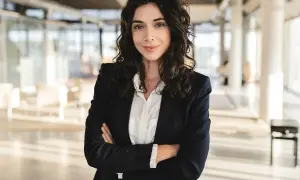 Kobieta w eleganckim business attire, z rękami skrzyżowanymi na piersi, pewnie patrzy w obiektyw.