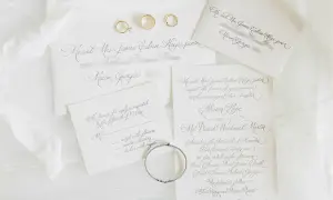 Eleganckie zaproszenia ślubne z kopertami i obrączkami. Widać, jak napisać zaproszenie z osobą towarzyszącą, z miejscem na wpisanie gościa.