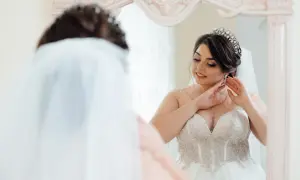 Panna młoda w pięknej sukni ślubnej z tiulowym dołem i zdobionym gorsetem poprawia kolczyk. Wymiary sukni ślubnej są idealne.