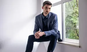 Elegancki mężczyzna w granatowej koszuli i marynarce, zastanawia się, jakie spodnie do niebieskiej koszuli będą najlepsze.