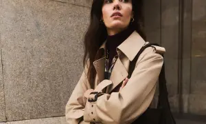 Elegancka kobieta w beżowym trenczu, klasycznym okryciu wierzchnim, pozuje na tle miejskiej ściany.