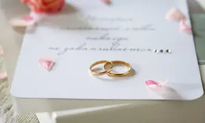 Eleganckie zaproszenie z osobą towarzyszącą, ozdobione płatkami róż i złotymi obrączkami.