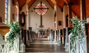Elegancka dekoracja kościoła na ślub samemu: ławki ozdobione zielenią i lampionami, ołtarz z kwiatami.