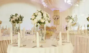 Elegancka sala weselna z białymi kwiatami i świecami. Stoły nakryte, gotowe na przyjęcie gości. Wiele pytań o szczegóły dekoracji sali weselnej.