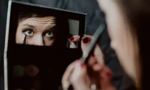 Kobieta wykonuje makijaż wieczorowy, precyzyjnie rysując kreskę eyelinerem na oku.