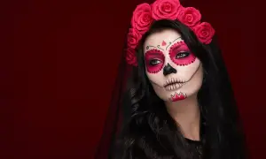 Kobieta z makijażem na halloween w stylu Catriny, ozdobiona czerwoną opaską z róż i welonem.