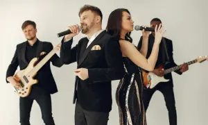 Zespół muzyczny w eleganckich strojach, wokalista i wokalistka śpiewają do mikrofonów, a gitarzyści grają na instrumentach. Idealni do oprawy muzycznej wesel i imprez, wykonają najlepsze przyśpiewki weselne.