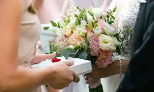 Dłoń podaje prezent ślubny, obok bukiet. Zastanawiasz się, ile dać na ślub cywilny?