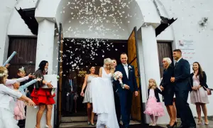 Para młoda wychodzi z kościoła, obsypana konfetti. Panna młoda ma na sobie białą suknię, pan młody granatowy garnitur. To piękny widok czegoś pozyczonego na ślub.
