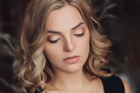 Delikatny, świąteczny makijaż podkreśla urodę blondynki. Jasne cienie na powiekach i subtelna szminka tworzą idealny look na zimowe przyjęcia.