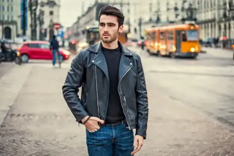 Młody mężczyzna w skórzanej kurtce i jeansach, stylizacja nawiązująca do moda męska lata 90. na tle miejskiej ulicy.