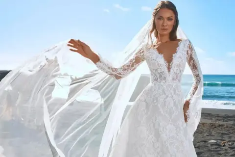 Piękna panna młoda w koronkowej sukni z długim rękawem i welonem na plaży. To marzenie każdej panny młodej.
