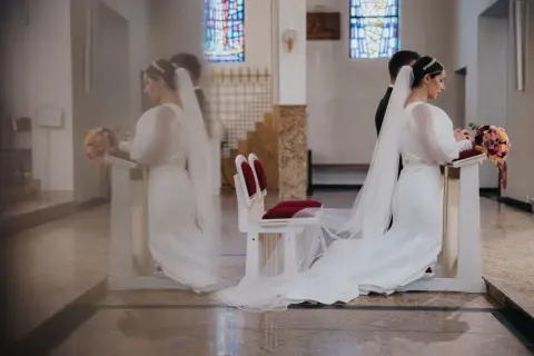Panna młoda w białej sukni i welonie klęczy przy ołtarzu, trzymając bukiet. To symboliczny moment przenoszenia przez próg nowego życia.