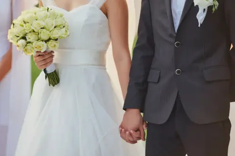 Para weselna trzymająca się za ręce. Panna młoda w białej sukni z bukietem róż. Zastanawiasz się, ile dać na wesele od 4 osobowej rodziny?