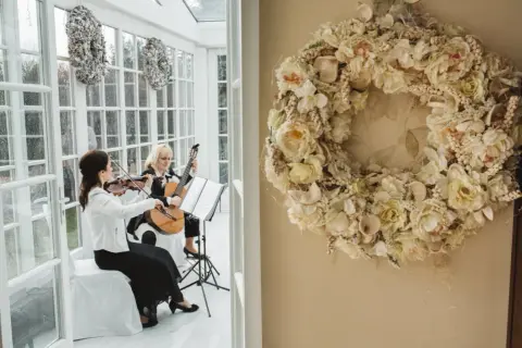 Elegancka oprawa muzyczna ślubu: skrzypaczka i gitarzystka tworzą magiczną atmosferę. Obok wianek z kwiatów.