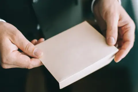 Dłonie trzymają jasnobrązowe pudełko. Czy osoba towarzysząca daje prezent?