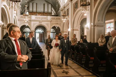 Para młoda idzie do wyjścia z kościoła, a goście śpiewają pieśń na wyjście z kościoła - ślub.