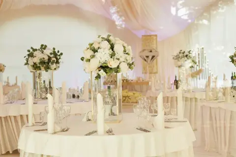 Elegancka sala weselna z białymi kwiatami i świecami. Stoły nakryte, gotowe na przyjęcie gości. Wiele pytań o szczegóły dekoracji sali weselnej.