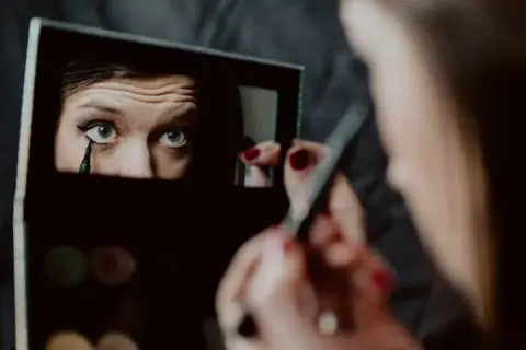 Kobieta wykonuje makijaż wieczorowy, precyzyjnie rysując kreskę eyelinerem na oku.