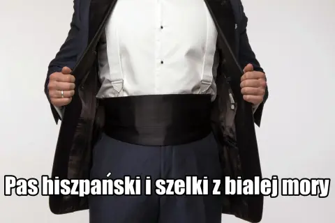 Elegancki mężczyzna w czarnym smokingu, białej koszuli i szelkach. Na brzuchu widoczny czarny pas do smokingu.
