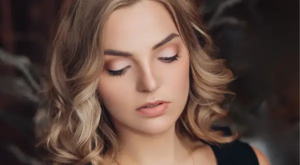 Delikatny, świąteczny makijaż podkreśla urodę blondynki. Jasne cienie na powiekach i subtelna szminka tworzą idealny look na zimowe przyjęcia.