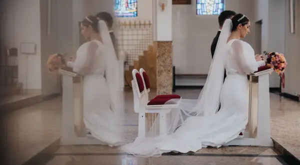 Panna młoda w białej sukni i welonie klęczy przy ołtarzu, trzymając bukiet. To symboliczny moment przenoszenia przez próg nowego życia.