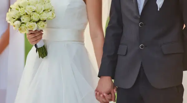 Para weselna trzymająca się za ręce. Panna młoda w białej sukni z bukietem róż. Zastanawiasz się, ile dać na wesele od 4 osobowej rodziny?