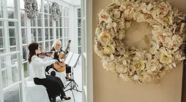 Elegancka oprawa muzyczna ślubu: skrzypaczka i gitarzystka tworzą magiczną atmosferę. Obok wianek z kwiatów.