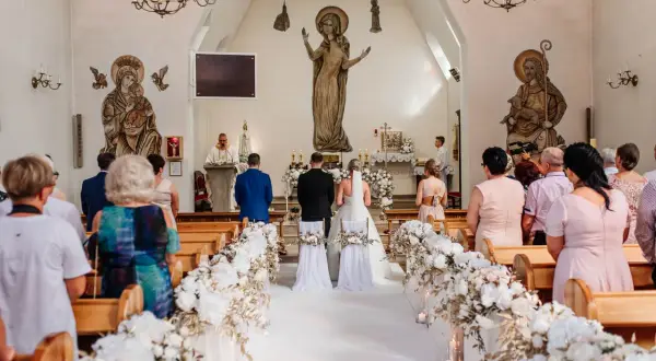 Przebieg mszy ślubnej: para młoda stoi przed ołtarzem w kościele, otoczona gośćmi i kwiatowymi dekoracjami.