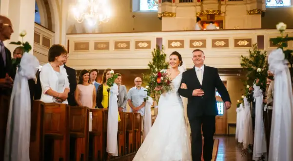 Przebieg ślubu kościelnego: panna młoda z bukietem idzie z ojcem do ołtarza, w kościele pełnym gości.