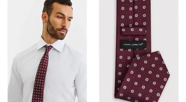 Mężczyzna w białej koszuli prezentuje bordowy krawat w białe wzory. Jego szerokość jest idealna do eleganckich stylizacji.