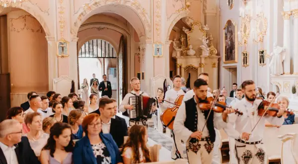 Muzycy grają pieśni na ofiarowanie ślub w kościele. W tle para młoda idzie do ołtarza.