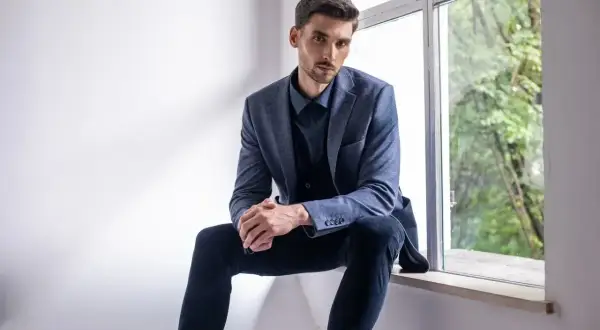Elegancki mężczyzna w granatowej koszuli i marynarce, zastanawia się, jakie spodnie do niebieskiej koszuli będą najlepsze.