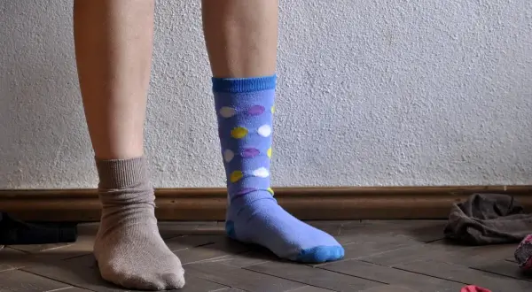 Dylemat: jakie skarpetki do jasnych spodni? Jedna stopa w beżowej, druga w niebieskiej w kropki.
