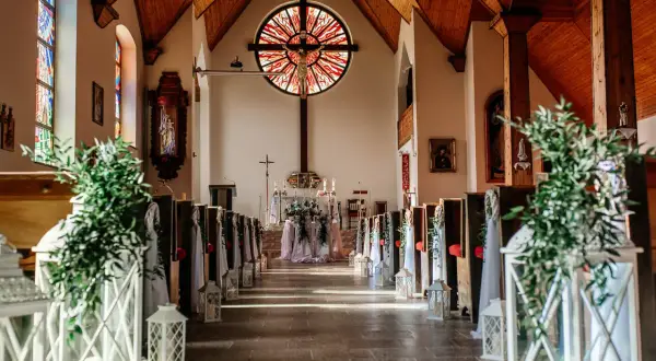 Elegancka dekoracja kościoła na ślub samemu: ławki ozdobione zielenią i lampionami, ołtarz z kwiatami.