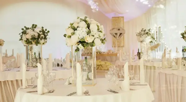 Elegancka sala weselna z białymi kwiatami i świecami. Stoły nakryte, gotowe na przyjęcie gości. Wiele pytań o szczegóły dekoracji sali weselnej.