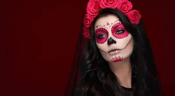 Kobieta z makijażem na halloween w stylu Catriny, ozdobiona czerwoną opaską z róż i welonem.