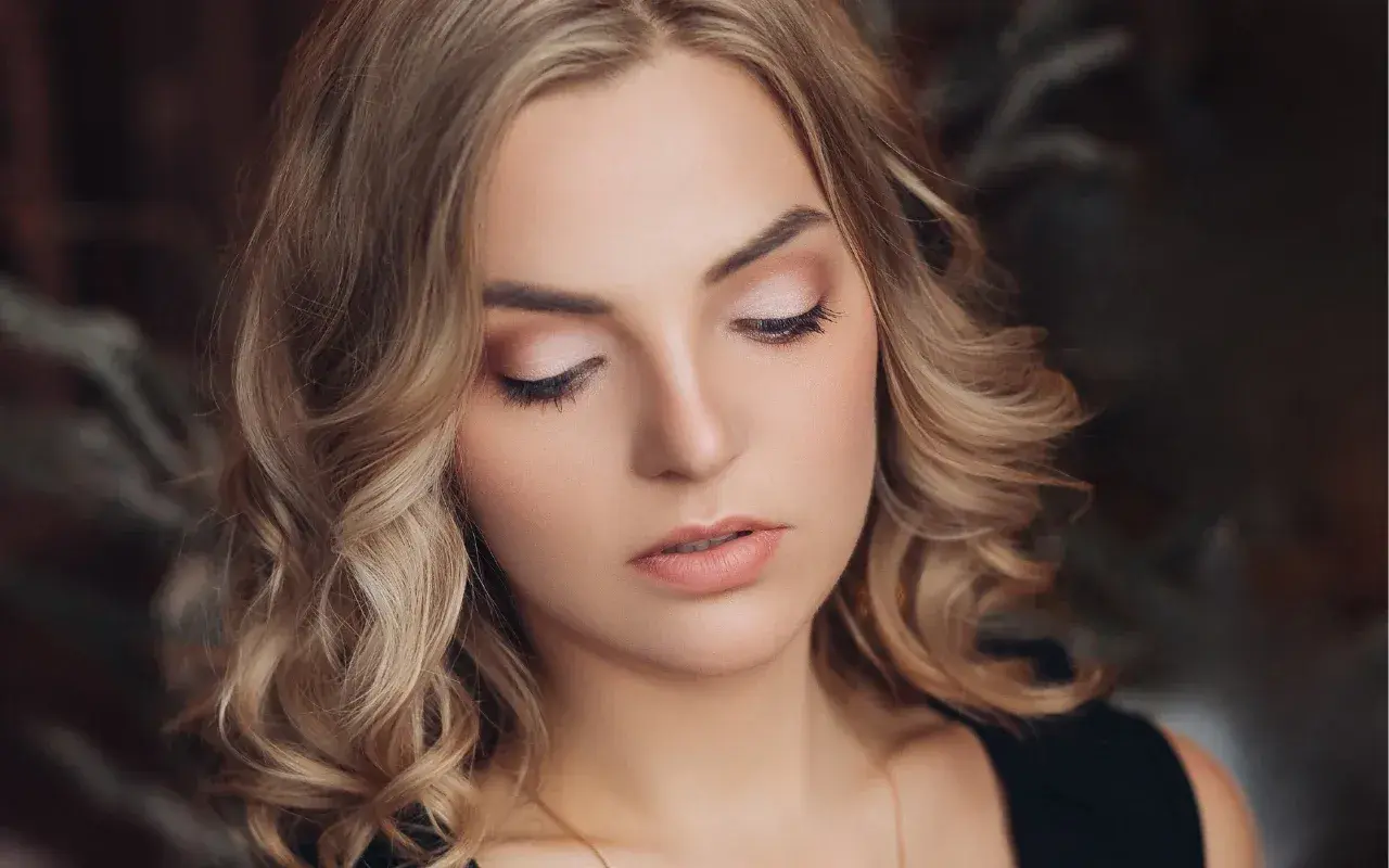 Delikatny, świąteczny makijaż podkreśla urodę blondynki. Jasne cienie na powiekach i subtelna szminka tworzą idealny look na zimowe przyjęcia.